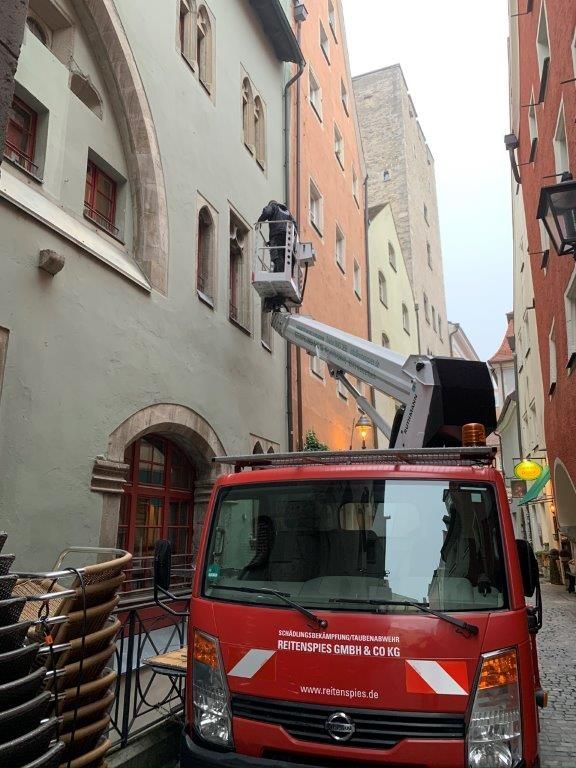 Roter Gabelstapler wartet ein Gebäude in einer engen Straße, Person im Hubkübel. Gebäude in verschiedenen Farben.