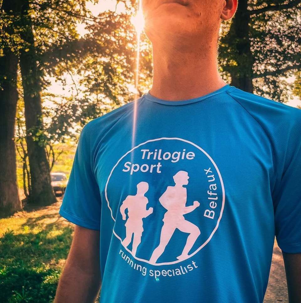 Homme en maillot de course bleu avec logo, décor extérieur ensoleillé.