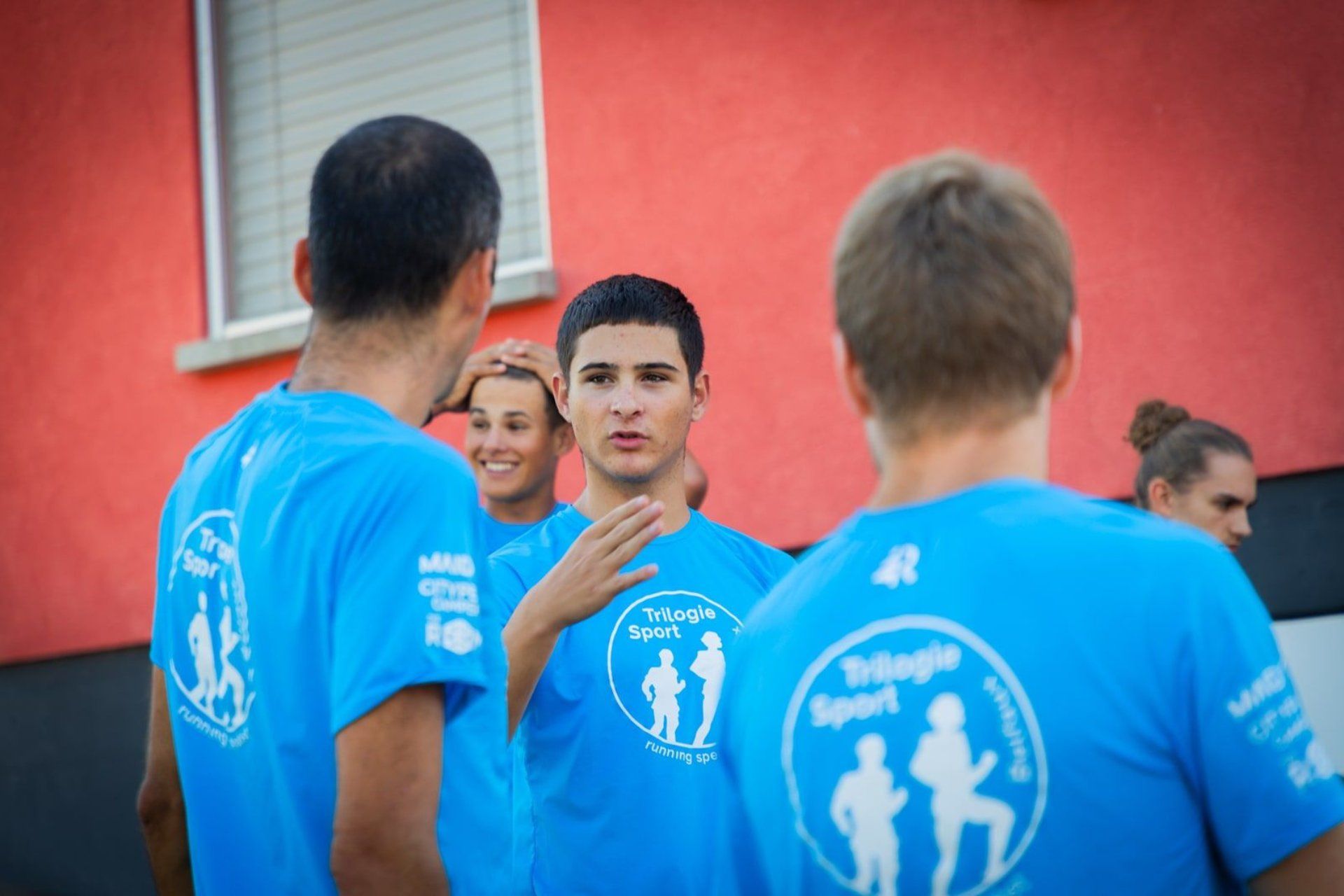 Des personnes vêtues de chemises bleues à logo discutent devant un mur rouge.