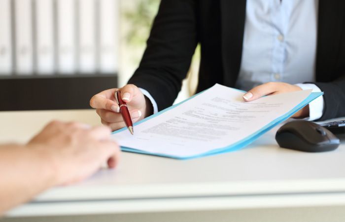 Una persona está sentada en un escritorio firmando un documento con un bolígrafo.