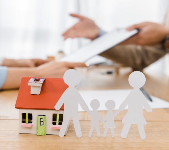 Un recorte de papel de una familia parada junto a una casa modelo.