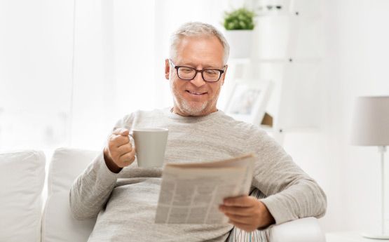 Un hombre está sentado en un sofá leyendo un periódico y tomando café.