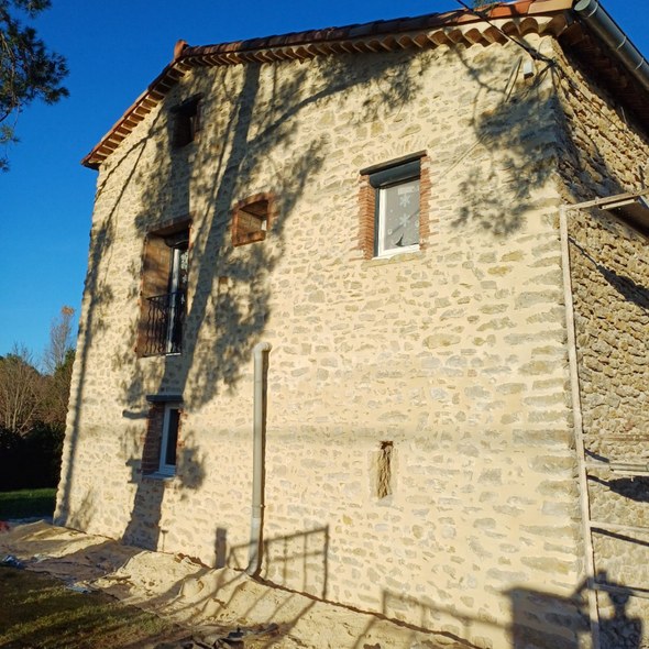 Façade d'un immeuble en pierre avec échafaudage et une personne travaillant