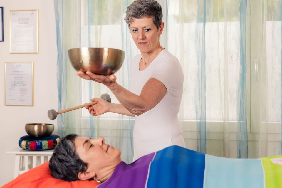 Eine Person benutzt während einer Spa-Massage eine Klangschale, wobei eine dunkle Schale und ein Klöppel über einem bäuchlings liegenden Kunden platziert werden.