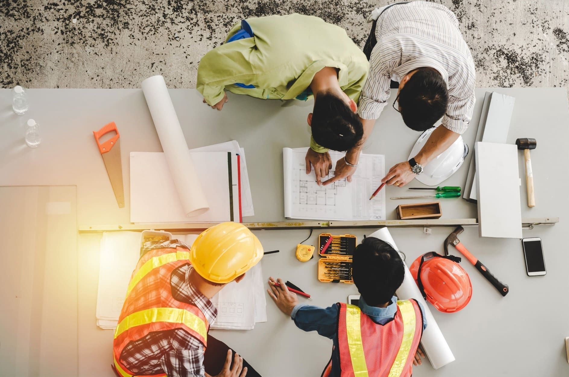 Un grupo de trabajadores de la construcción están sentados alrededor de una mesa mirando un plano.