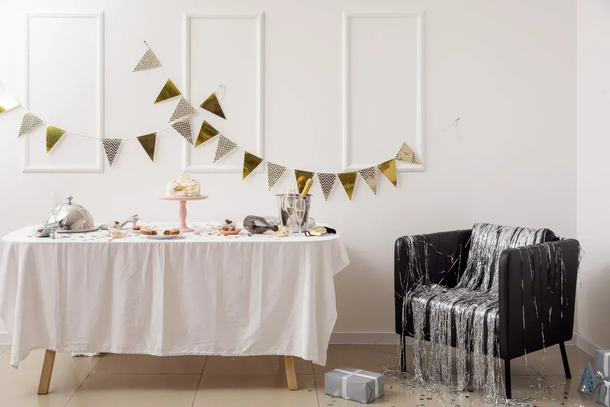 Escena de fiesta: Mesa con golosinas, decoraciones y una silla cubierta con serpentinas plateadas.