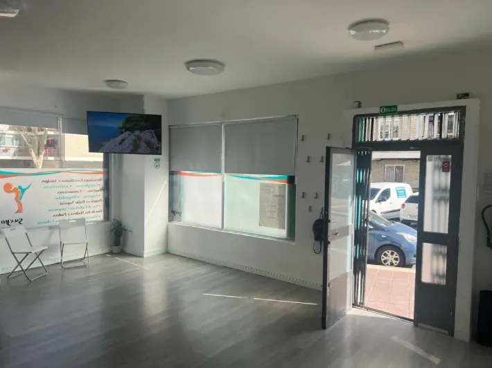 Habitación vacía y bien iluminada con la puerta abierta. Suelo gris, paredes blancas, televisor en la pared