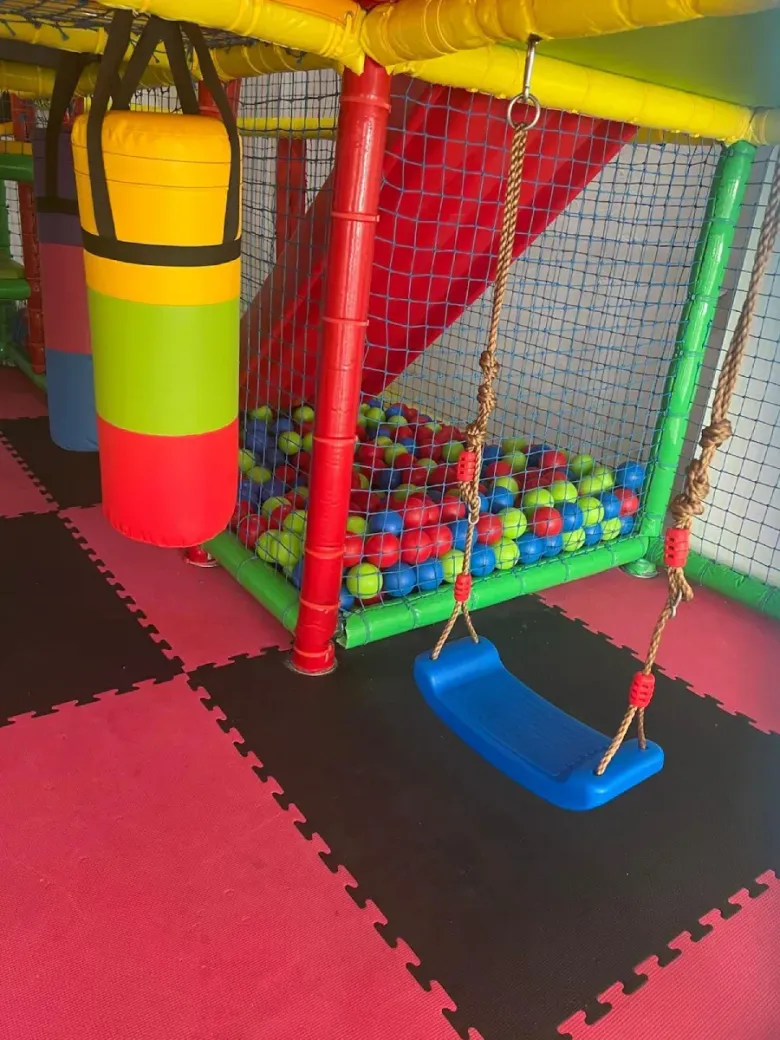 Zona de juegos interior colorida con colchonetas de espuma, piscina de bolas y un columpio azul