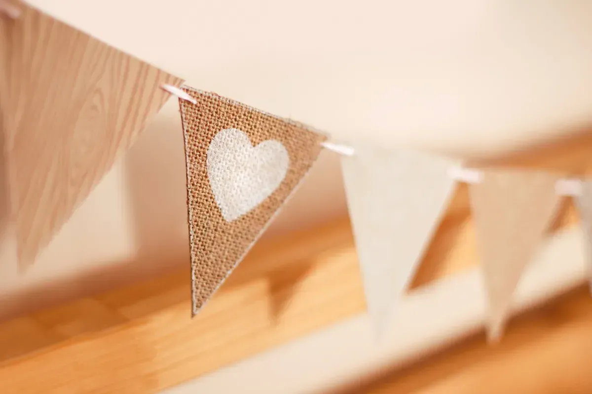 Bandera de arpillera con corazón blanco, para colgar en el interior, junto a otras banderas triangulares blancas y beige.