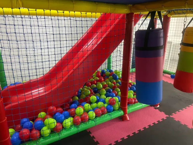 Zona de juegos interior colorida con colchonetas de espuma, piscina de bolas y un columpio azul