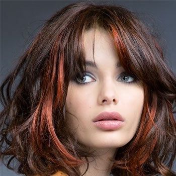 Un primer plano del rostro de una mujer con cabello castaño y reflejos rojos.