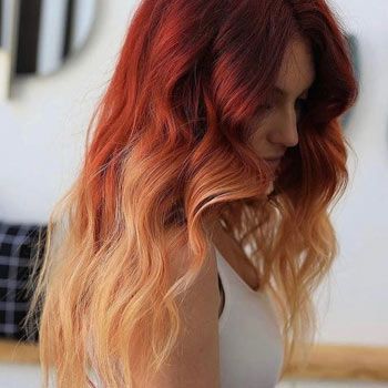 Una mujer con cabello largo rojo y rubio lleva una camiseta blanca sin mangas.