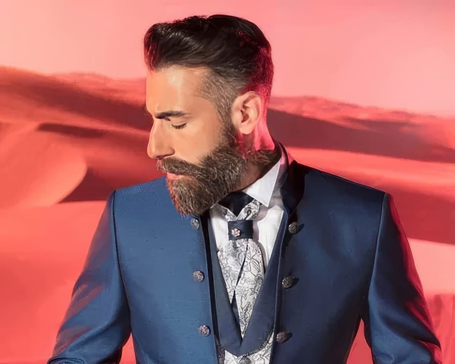 Un hombre con barba lleva un traje azul y corbata.