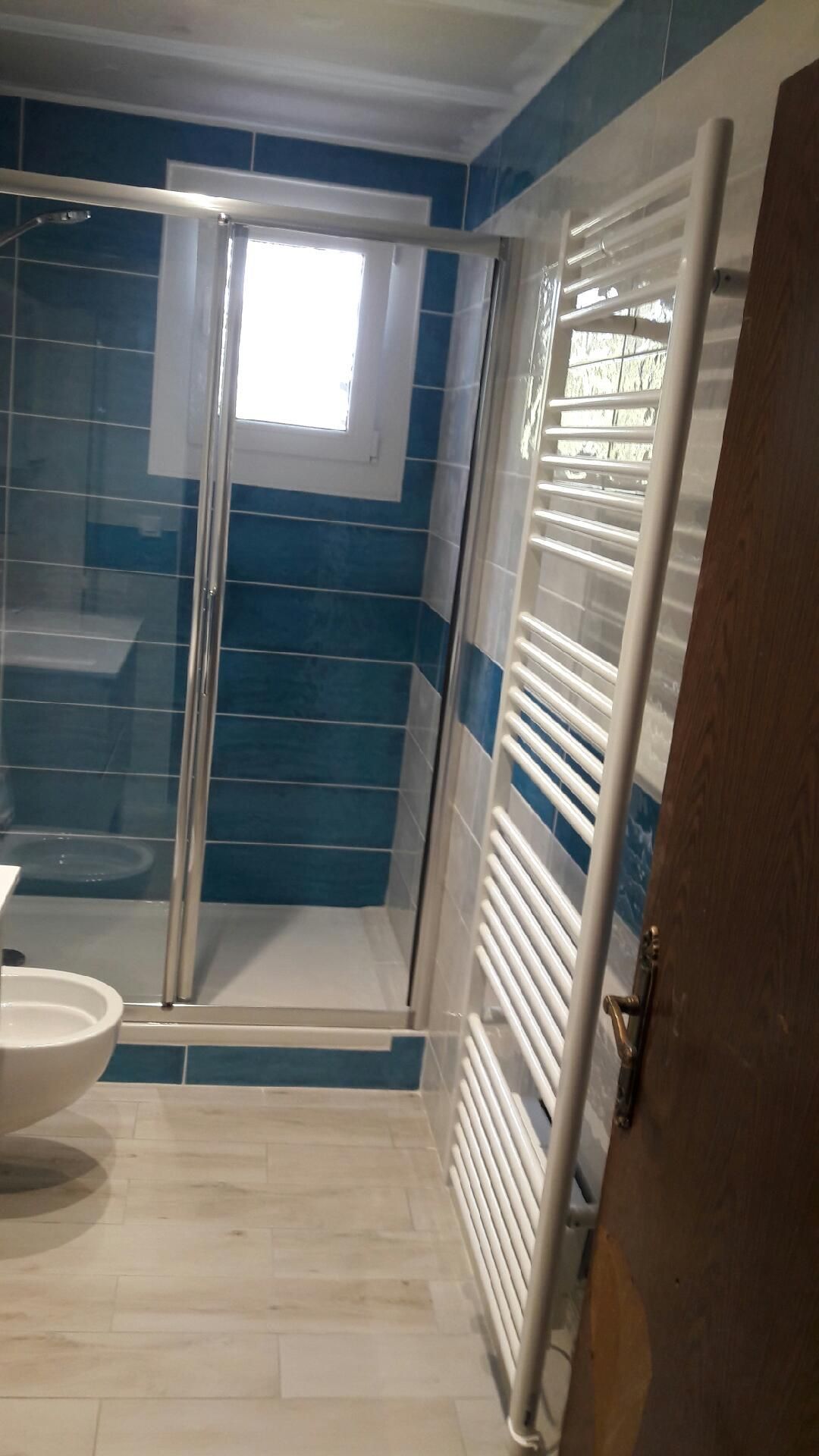 Salle de bains avec murs carrelés bleus, porte de douche en verre et sèche-serviettes blanc