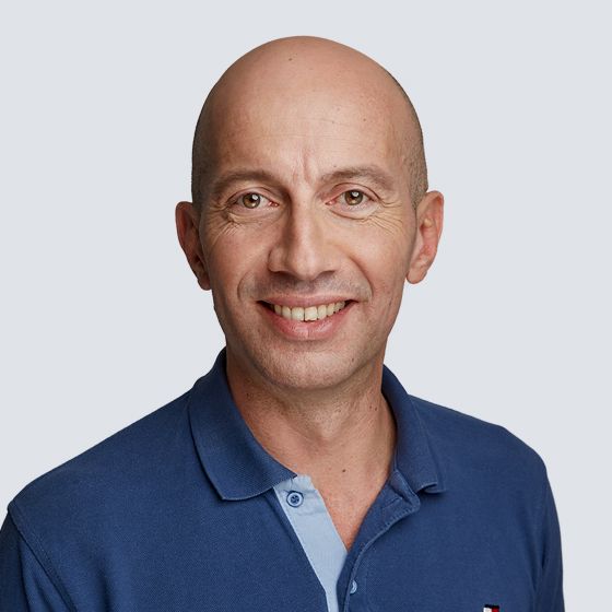 Glatzköpfiger Mann im blauen Poloshirt lächelt, Porträt (Kopf und Schultern).