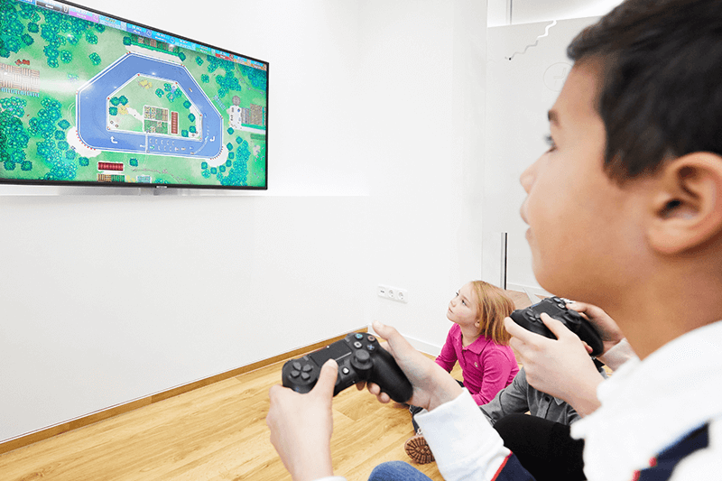 Drei Kinder spielen ein Videospiel auf einem großen Fernseher, eines hält einen Controller.