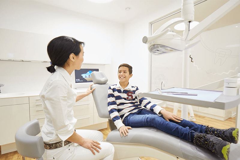 Zahnarzt und Patient in einer Zahnarztpraxis; beide lächeln. Der Patient sitzt auf dem Zahnarztstuhl.