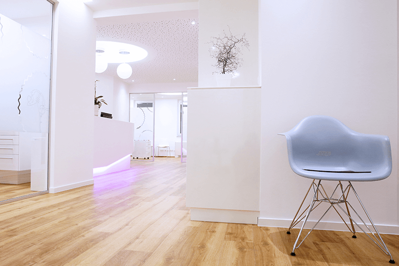 Ein hellblauer Stuhl in einem modernen Zahnarztpraxisflur mit Holzboden und weißen Wänden.