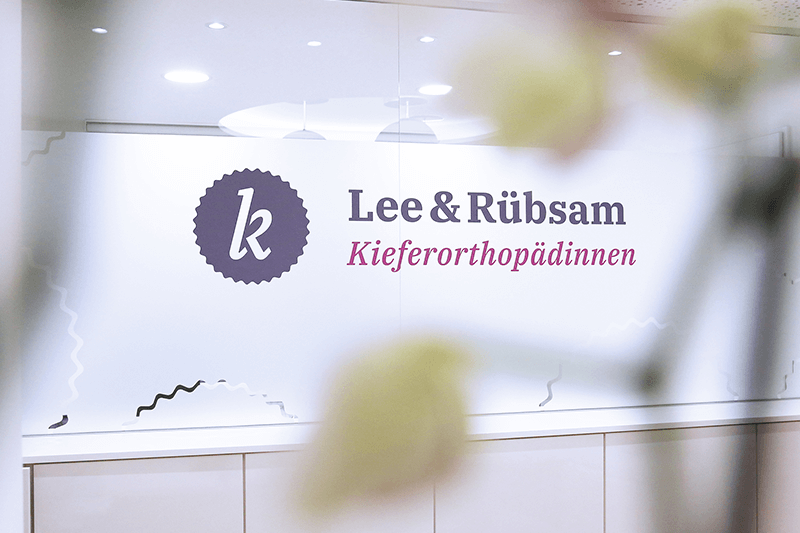 Lee & Rübsam – Büroschild der Kieferorthopädiepraxis auf Glas mit Logo.