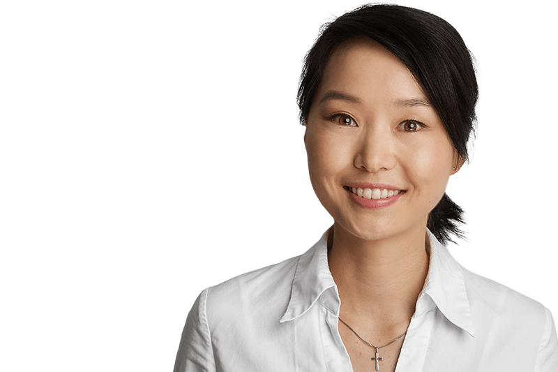 Eine Frau mit dunklen Haaren lächelt. Sie trägt ein weißes Hemd und eine Halskette.