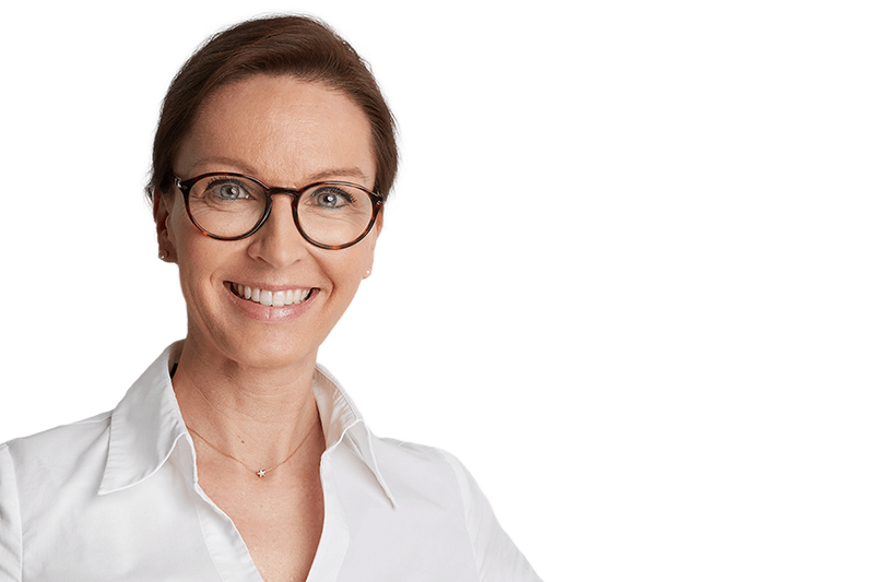 Frau mit Brille lächelt, trägt ein weißes Hemd; vor weißem Hintergrund.