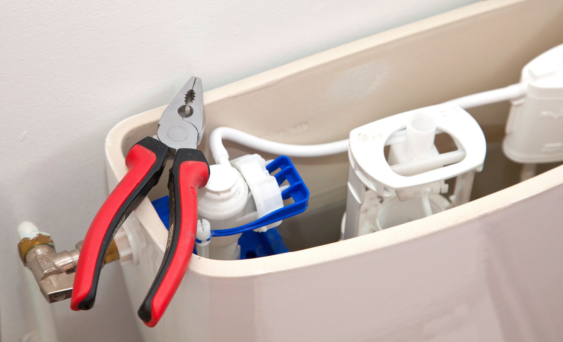 Ouvrez le réservoir des toilettes avec une pince à poignée rouge à côté du mécanisme de chasse d'eau et des pièces de la valve bleue.