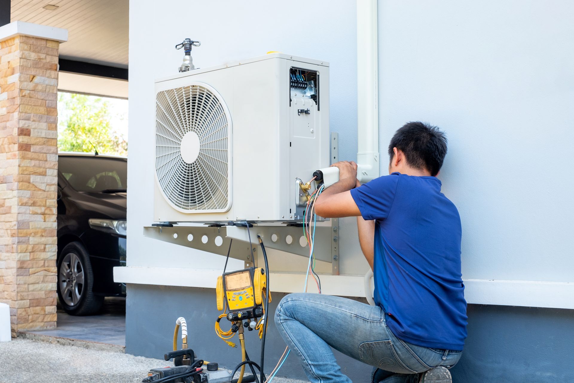 Un technicien agenouillé à côté d'un climatiseur extérieur, utilise des outils pour le réparer.