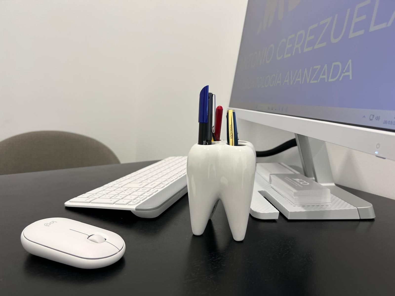Un portalápices con forma de diente se encuentra sobre un escritorio al lado de una computadora.