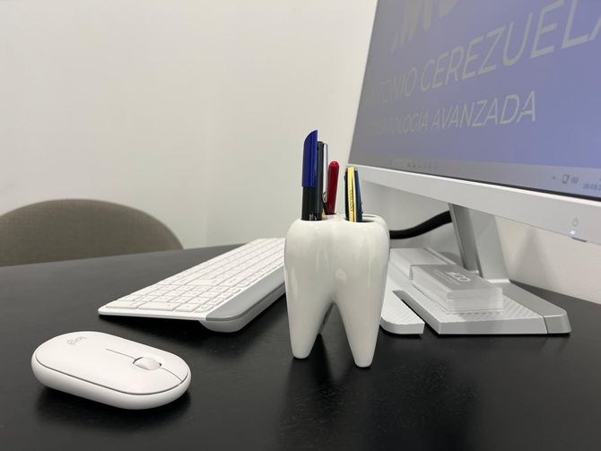 Un portalápices con forma de diente se encuentra sobre un escritorio al lado de una computadora.
