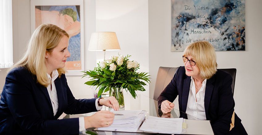 Zwei Frauen sitzen an einem Tisch und unterhalten sich.