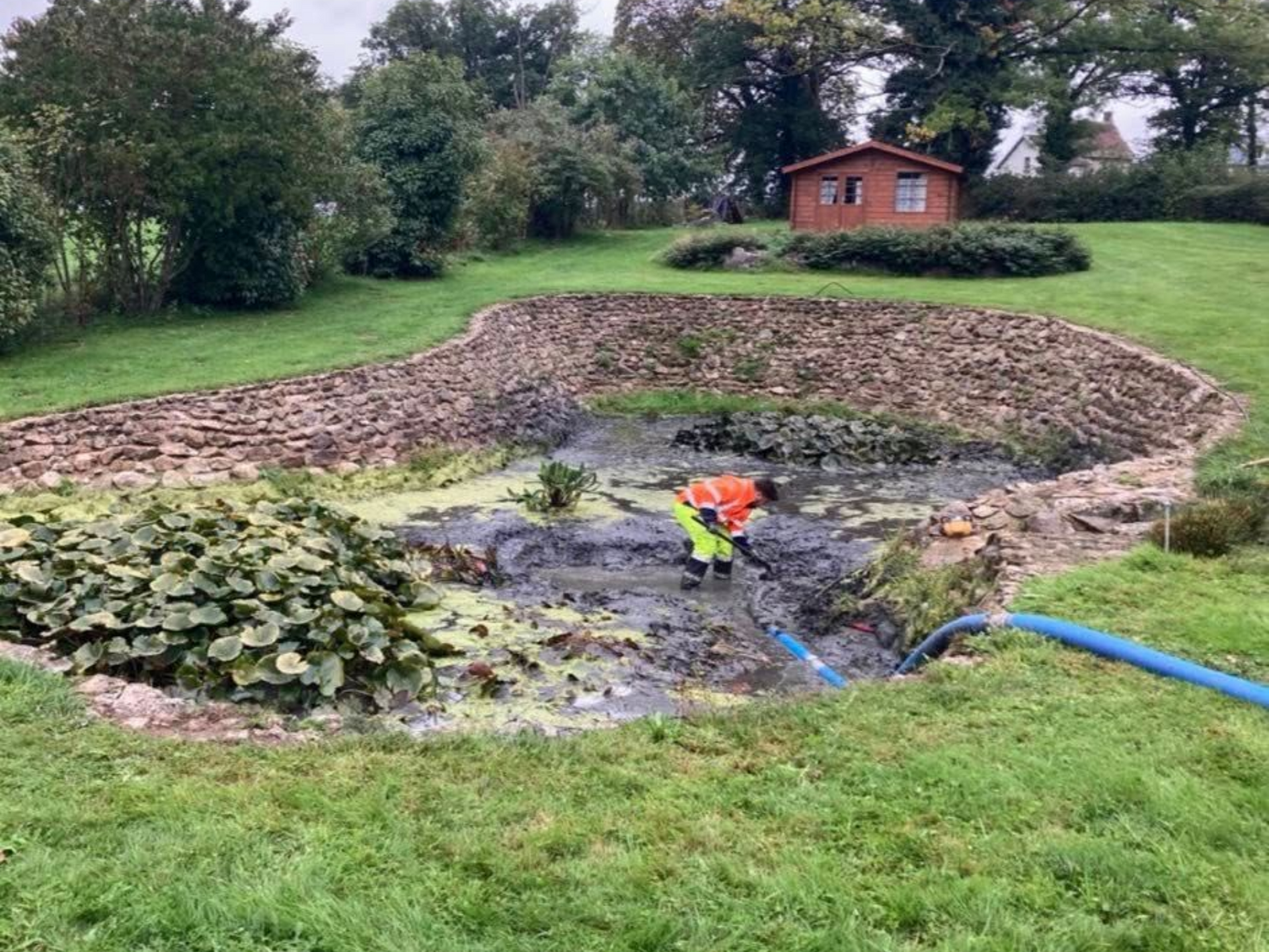 Un homme en combinaison orange nettoie un étang boueux.