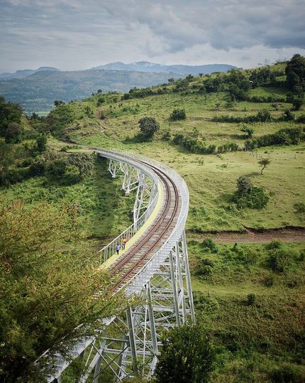 Curving elevated railway track through lush green hills under a cloudy sky