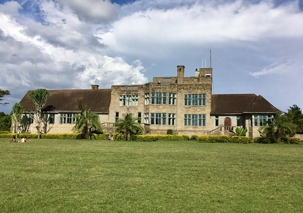 Large historic stone house with many windows and a wide green lawn under a cloudy sky