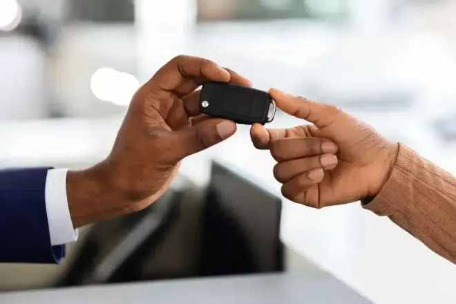 Two hands exchanging a black car key fob at a counter.