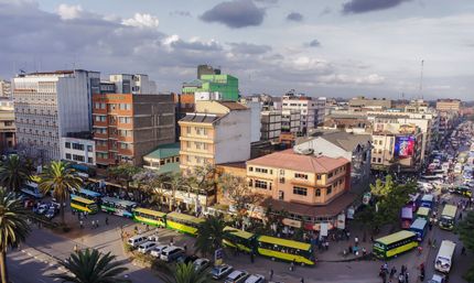 Busy city intersection with yellow buses, cars, and crowded buildings under a cloudy sky