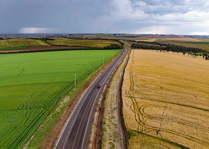 Aerial view of a winding road between green and golden farmland under a cloudy sky
