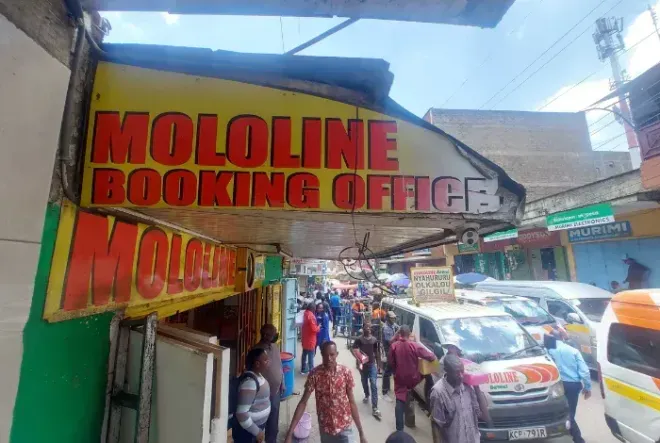Crowded street outside MOLoline Booking Office with people walking past storefronts and cars nearby