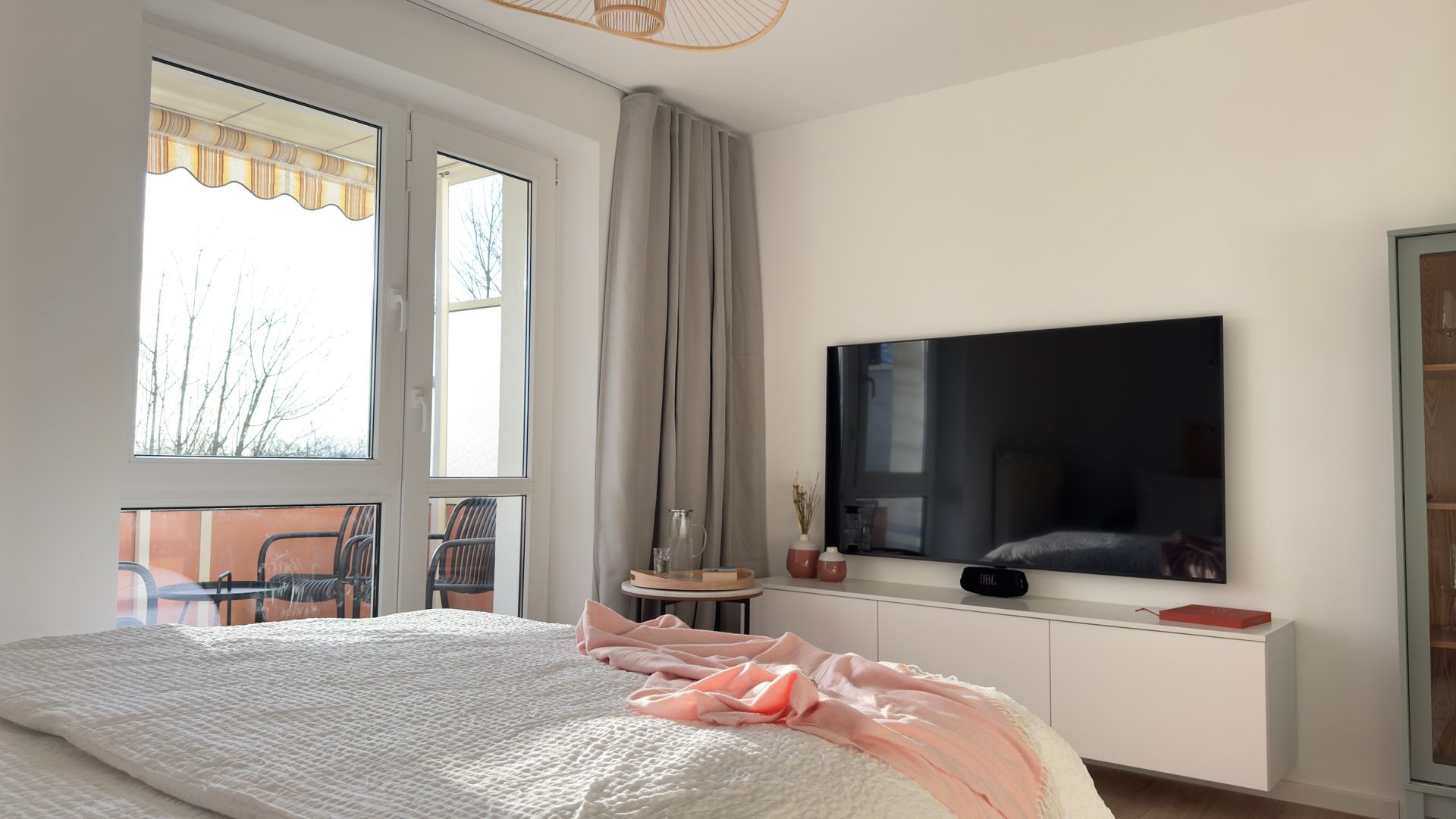 Fensterblick im Wohnbereich und Blick auf den TV und die Verdunklungsvorhänge vor dem Balkonfenster vom gemütlichen Schlafsofa.