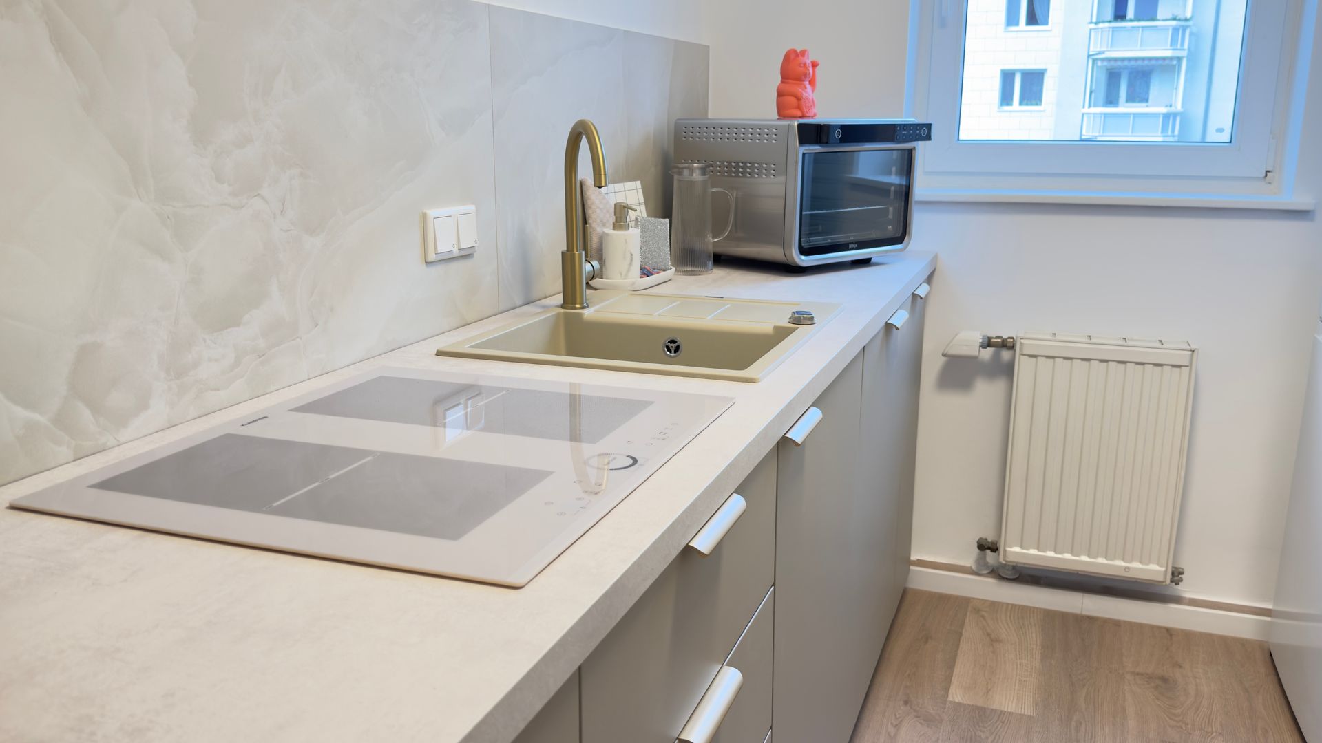 Küchendetail mit Spüle, Kochfeld, Multifunktionsofen und Fenster