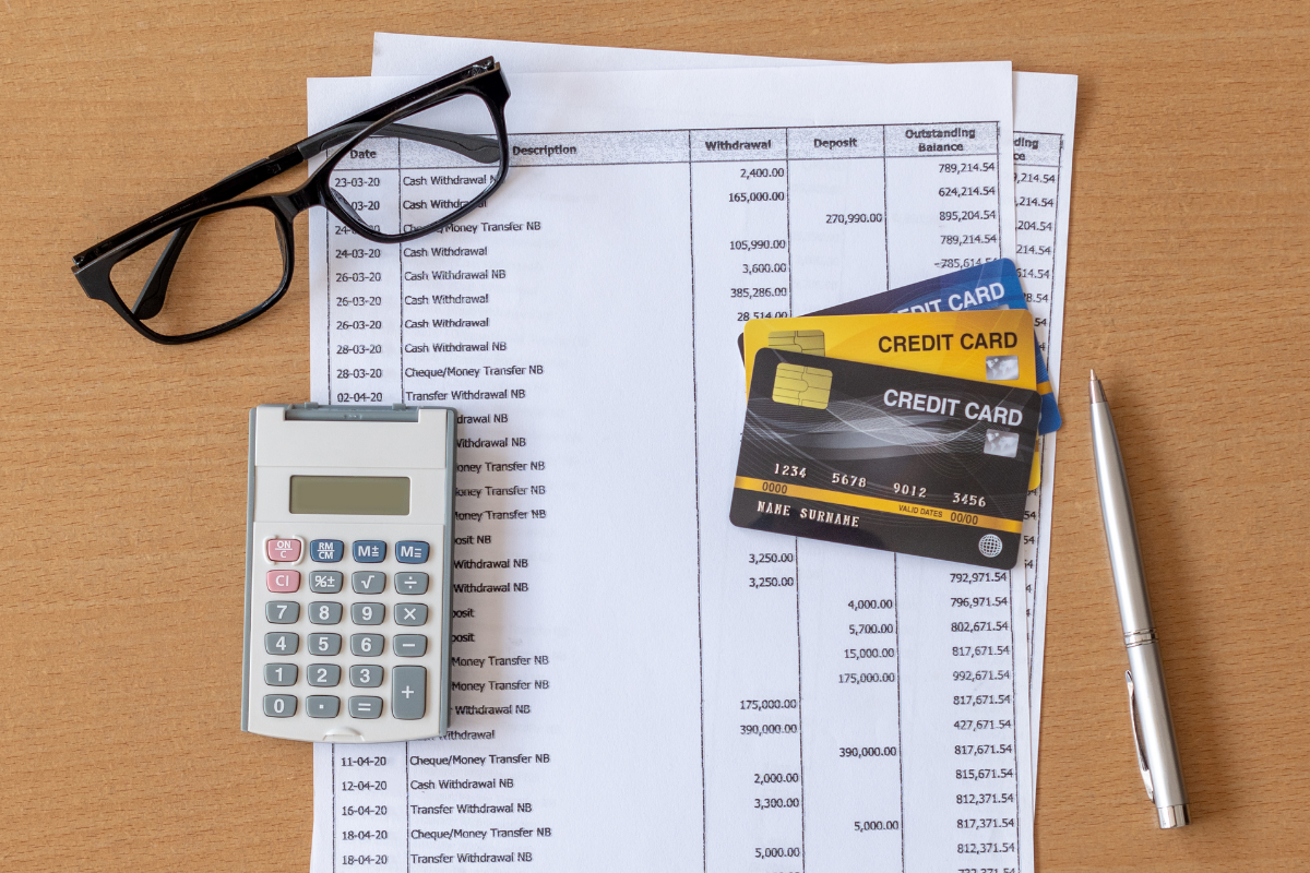 Calculatrice, lunettes, cartes de crédit et stylo sur des documents financiers.