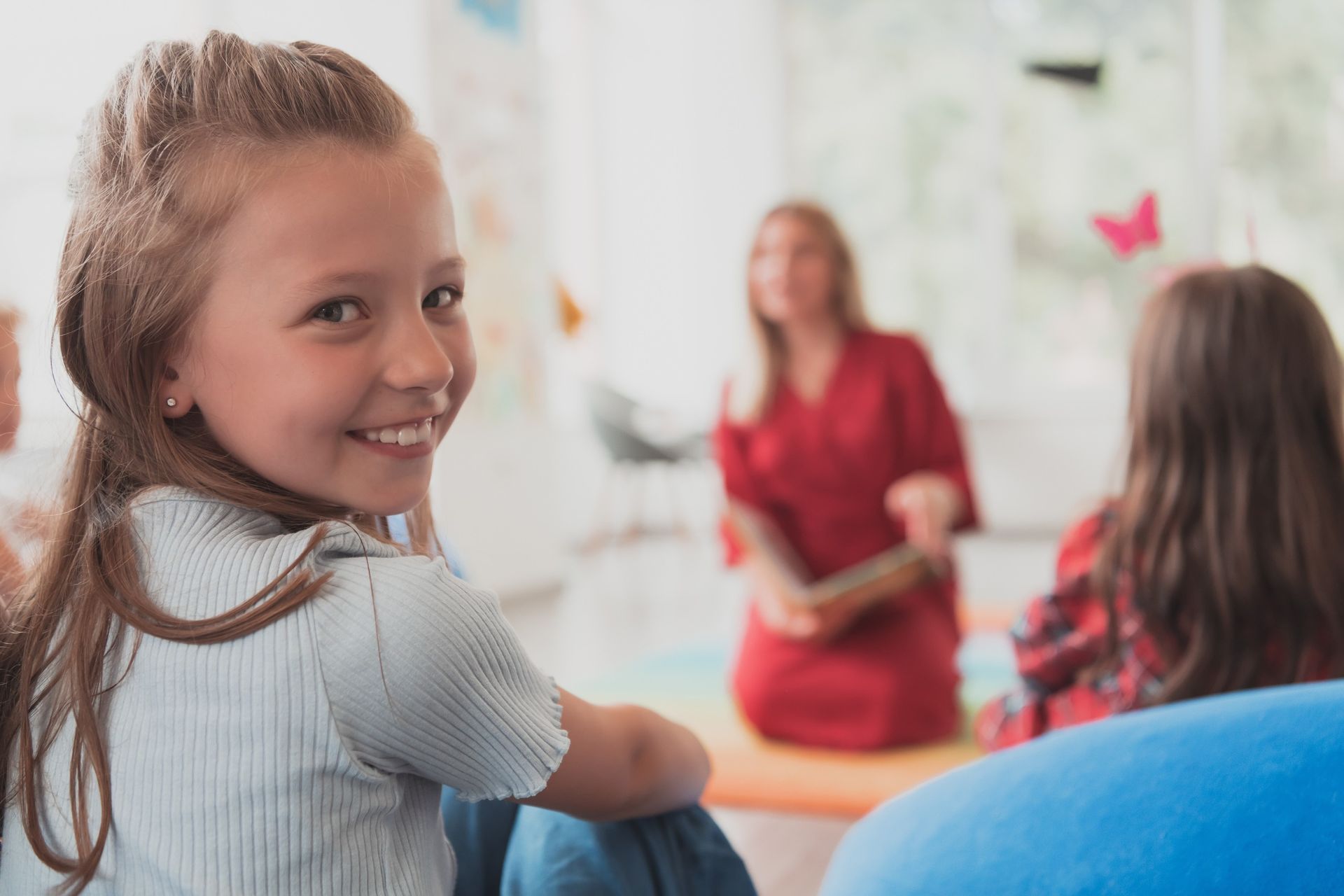 Una niña sonríe mientras está sentada en una silla en un salón de clases.