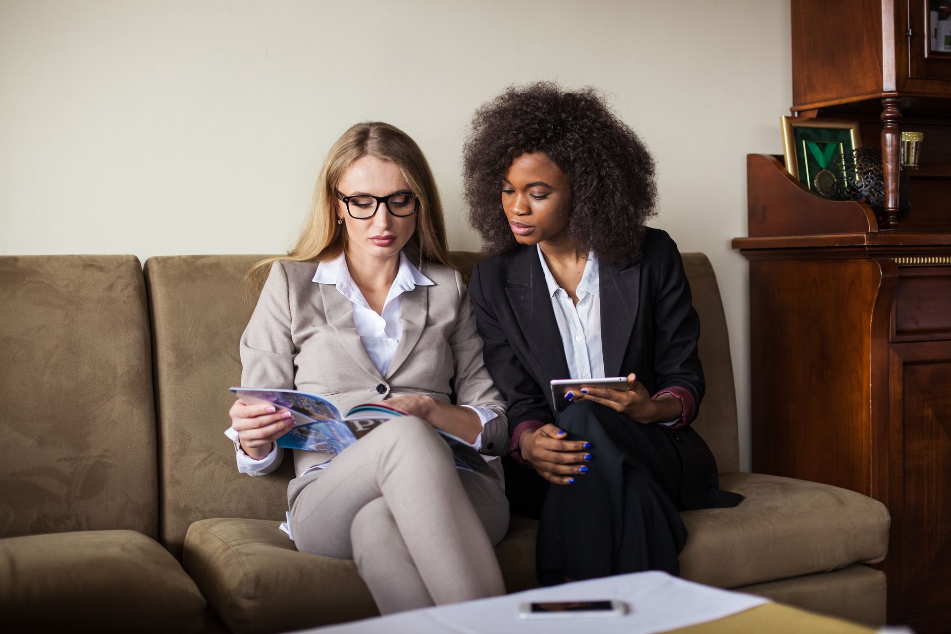 Dos mujeres están sentadas en un sofá mirando una revista.