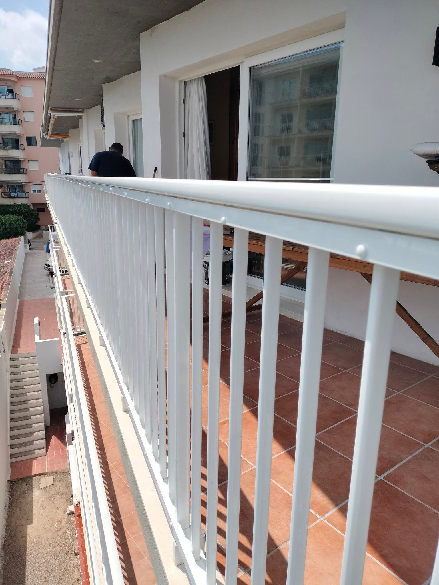 Balcón con barandilla blanca y baldosas de terracota, con vistas a los edificios cercanos 