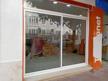 Escaparate cerrado con puerta corredera de cristal, marco naranja y desorden interior visible tras el reflejo.