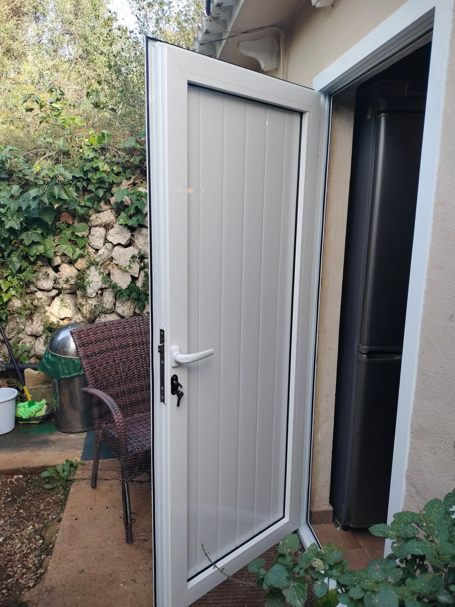 Puerta exterior blanca abierta que da a un patio ajardinado con plantas y losas de piedra.