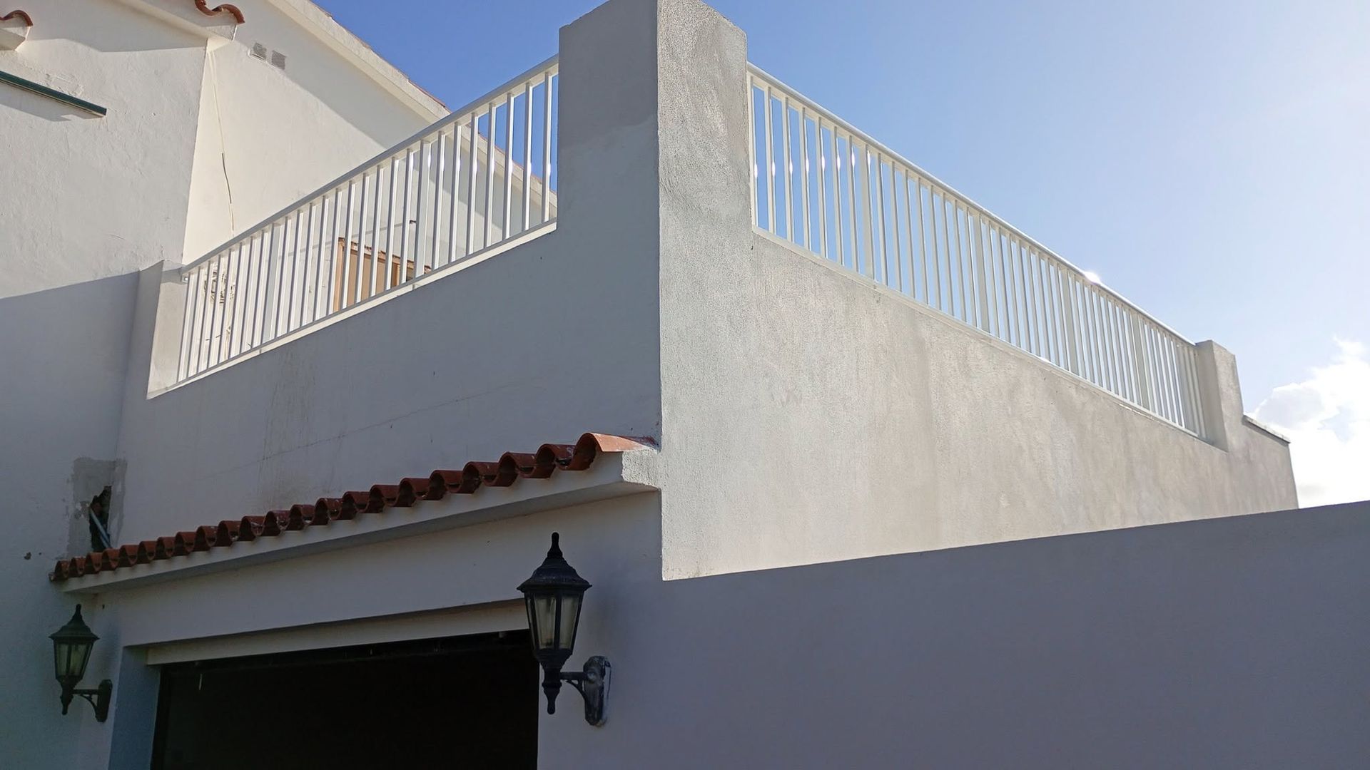 Casa de estuco blanco con terraza en la azotea, barandilla blanca y una linterna negra sobre la puerta.