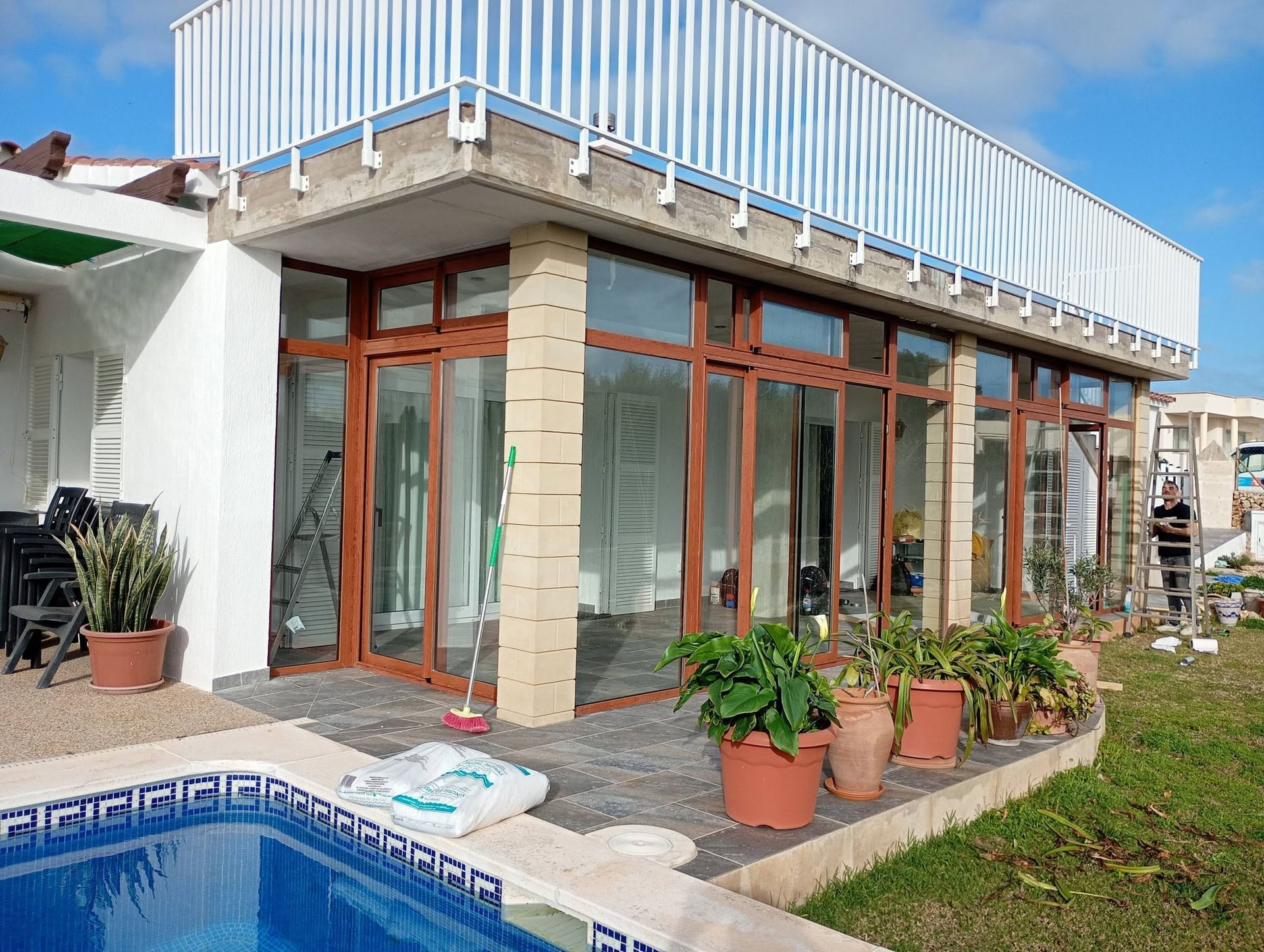 Exterior de una casa moderna con puertas de cristal, terraza en la azotea, plantas en macetas y una pequeña piscina.