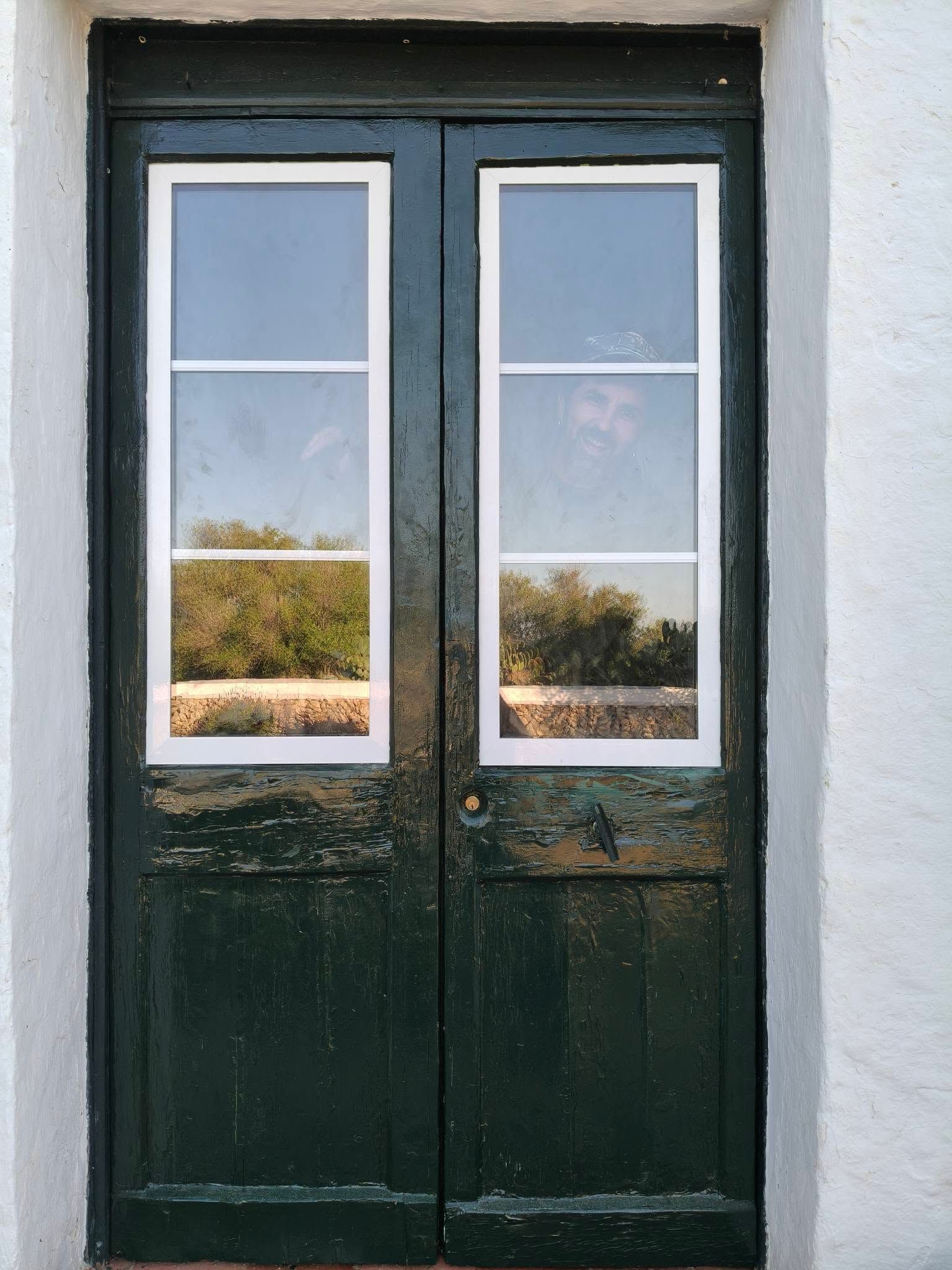 Puertas dobles de color verde oscuro con ventanas estrechas y molduras blancas.