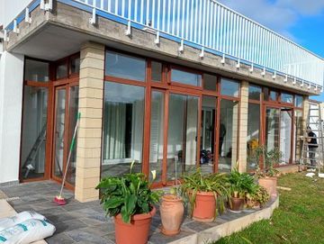 Patio de casa moderna con grandes puertas de cristal, plantas en macetas y un balcón en la planta superior.
