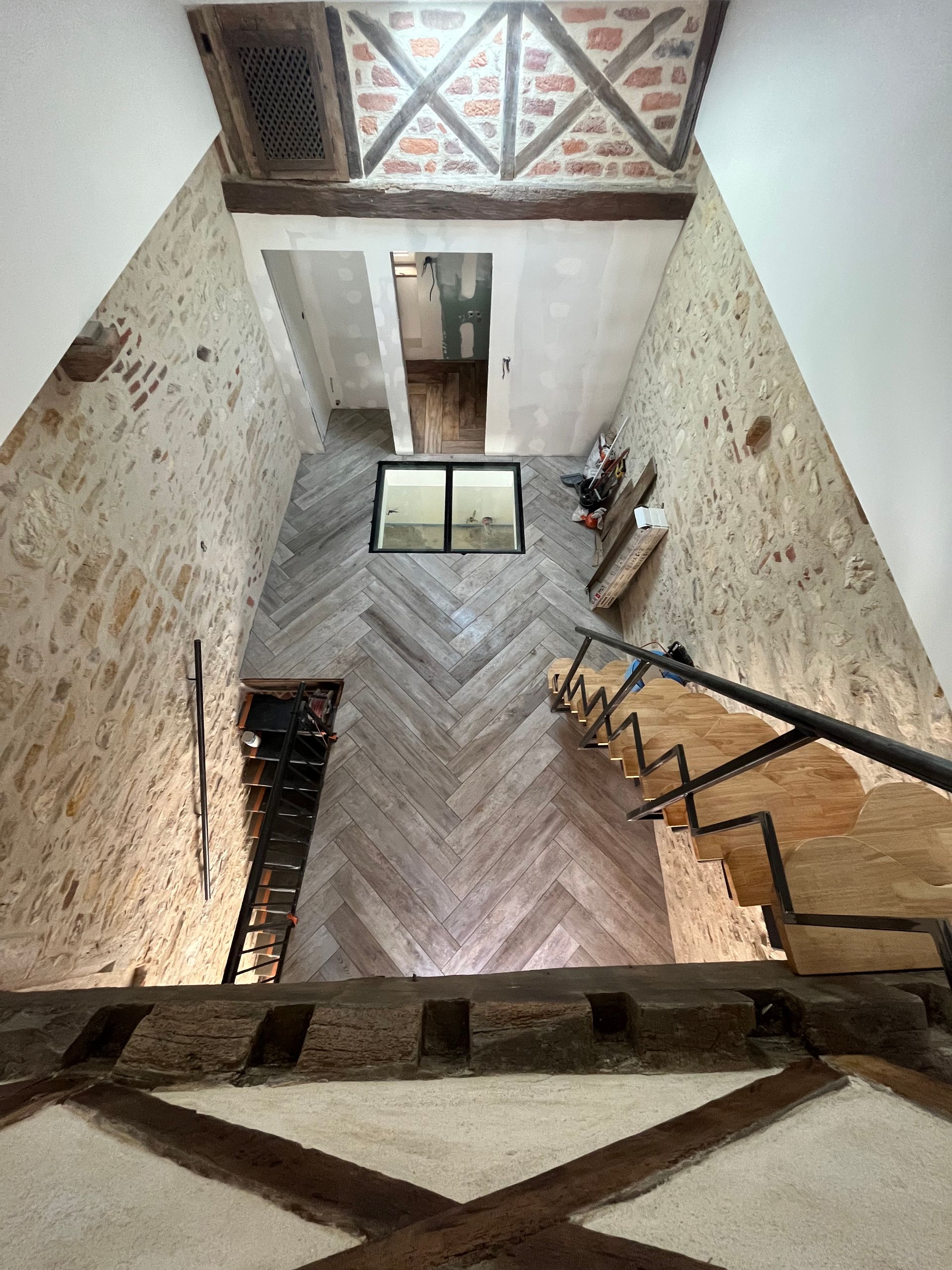 Photo vue de haut d'une pièce rénovée avec escalier en bois et mur en pierres apparentes